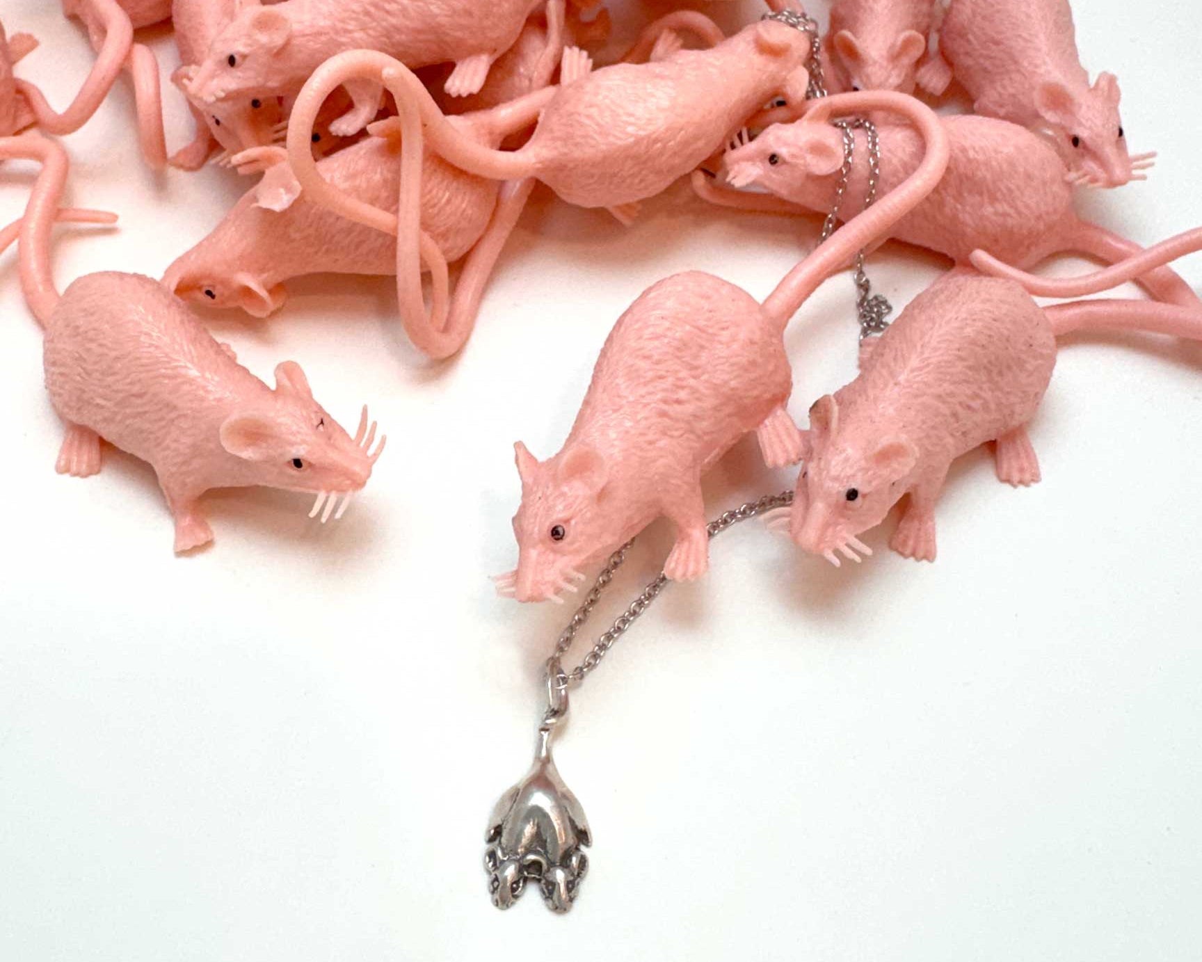 Pink rubber rat surrounding a two headed rat necklace in silver on a white background